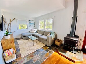 A cozy living room with a sectional sofa, a glass coffee table, a fireplace, and a stone-tiled floor. - Surf Break On Bruxner - Korora (Pet Friendly) (Korora)
