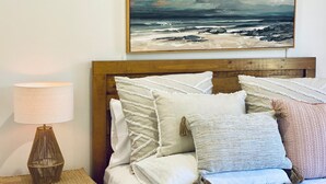 A bed with multiple pillows and a lamp on a bedside table, with a painting of a seascape above it. - Surf Break On Bruxner - Korora (Pet Friendly) (Korora)