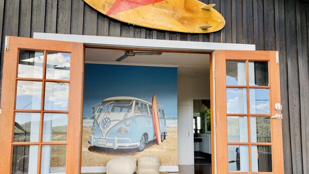 A wooden door with glass panels leading to a room with a beach-themed mural, a wooden floor, and a welcome mat. - Surf Break On Bruxner - Korora (Pet Friendly) (Korora)