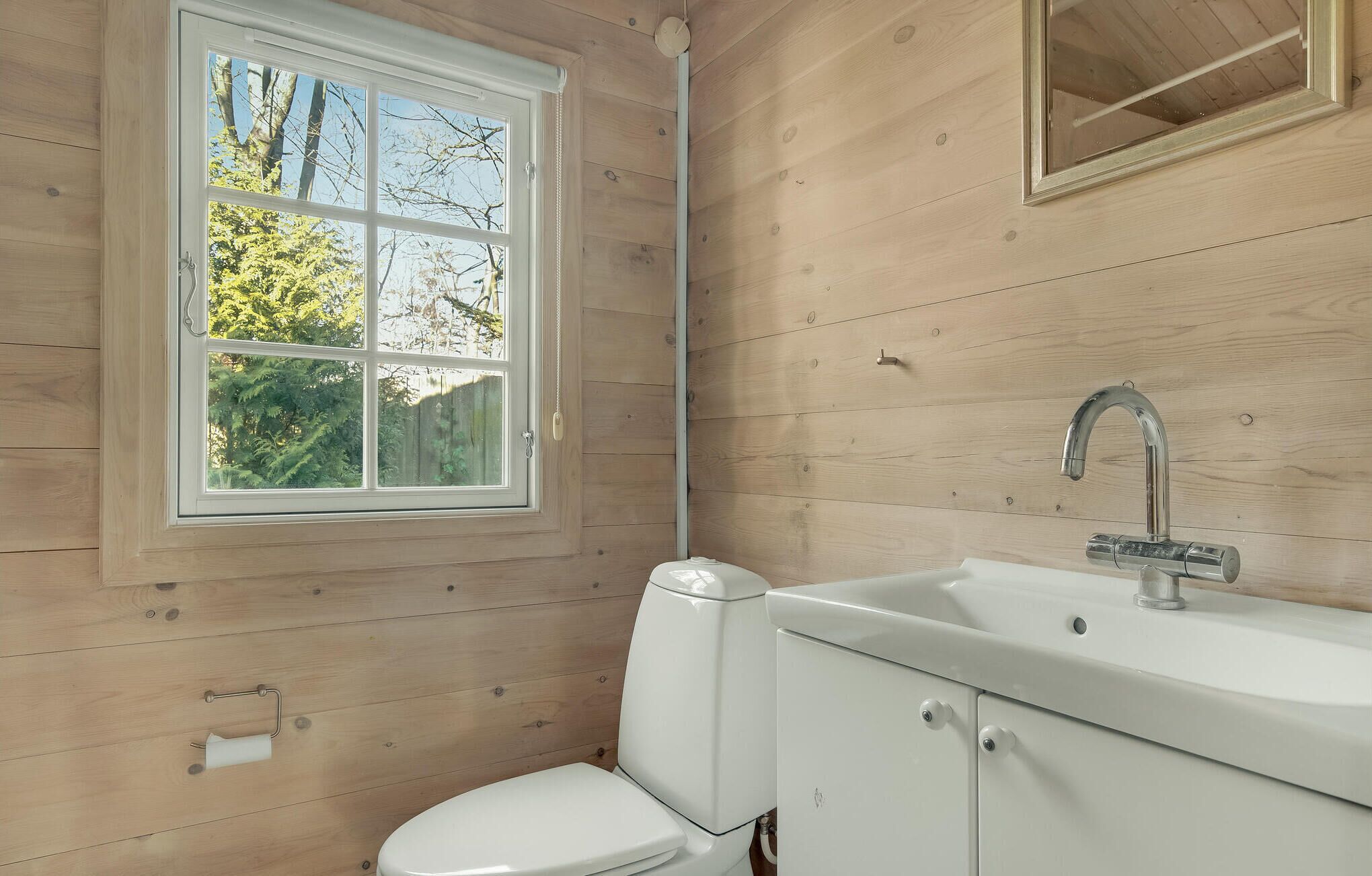 Un baño con pared de madera, una ventana, un inodoro y un lavabo con grifo.