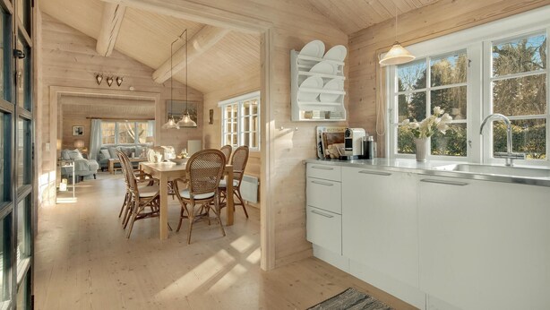 Un'ampia cucina con mobili bianchi, un'area pranzo con sedie in vimini e un'ampia finestra che offre luce naturale.
