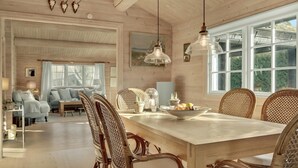 Un'ampia stanza con un grande tavolo da pranzo in legno, sedie in vimini e vista sull'esterno tramite ampie finestre.