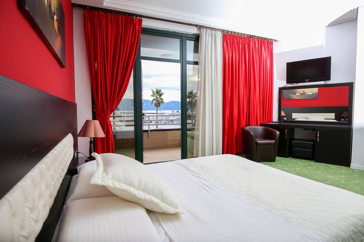 A hotel room with a bed, a desk, a television, and a view of the outdoors.