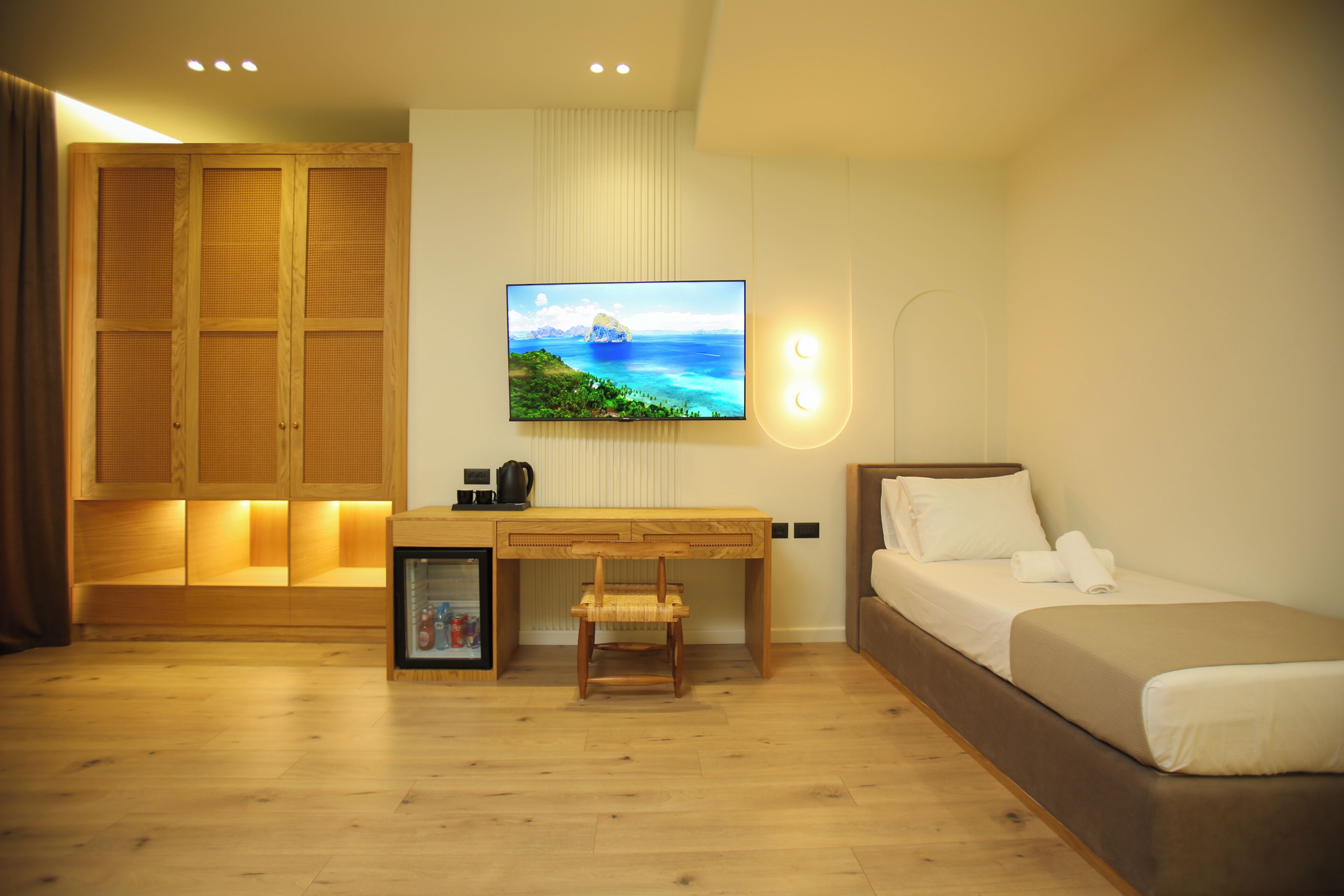 Una camera d'albergo con un letto, una scrivania con una sedia, una televisione a parete e un armadio.