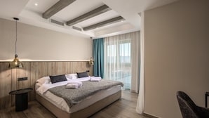 Ein modernes Hotelzimmer mit einem großen Bett, einem Nachttisch, einer Lampe und Blick ins Freie.
