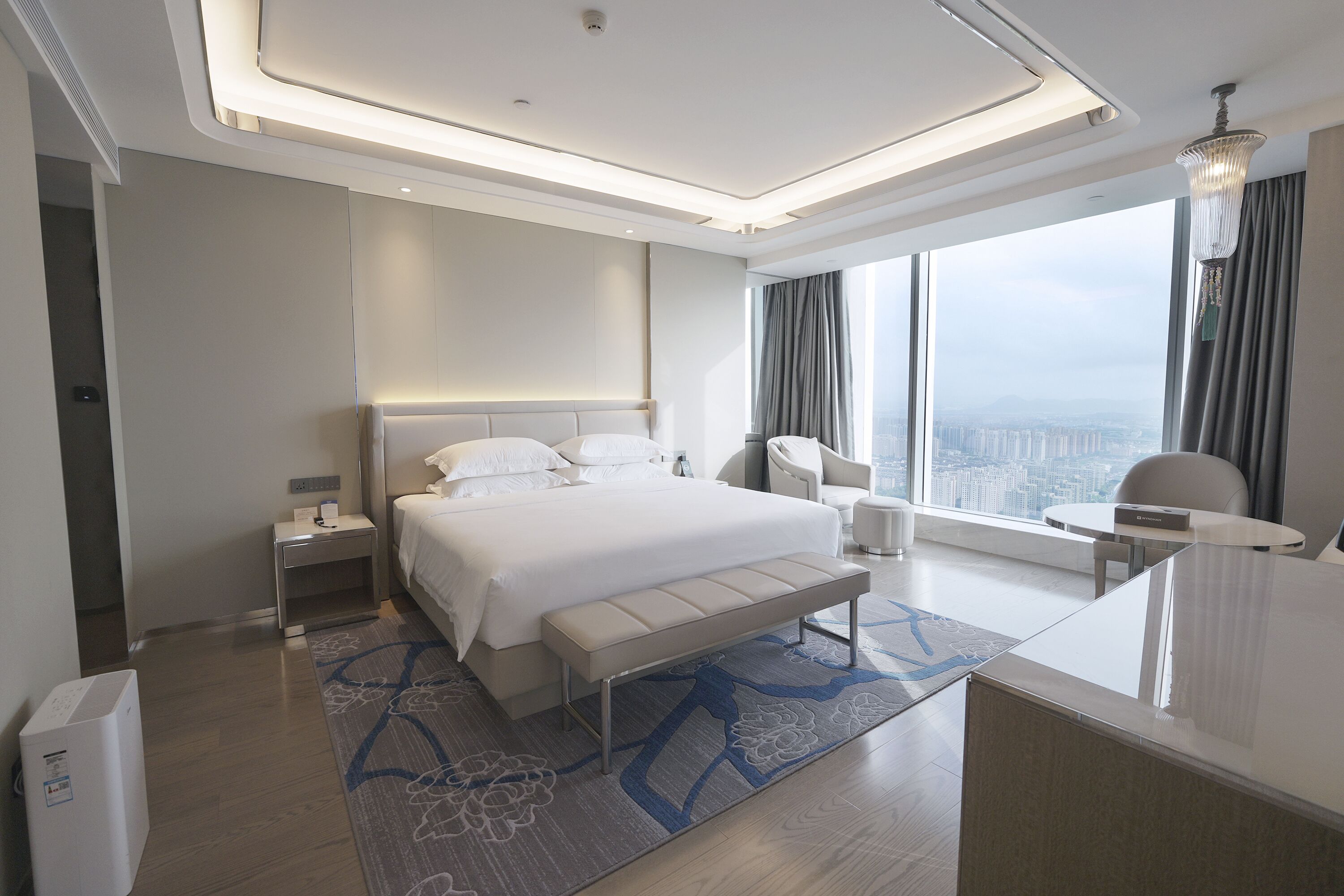 A modern hotel room with a large bed, bedside tables, a desk, and a view of the city.