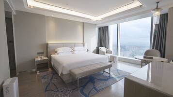 Habitación de hotel moderna con una cama grande, mesitas de noche, un escritorio y vistas a la ciudad.