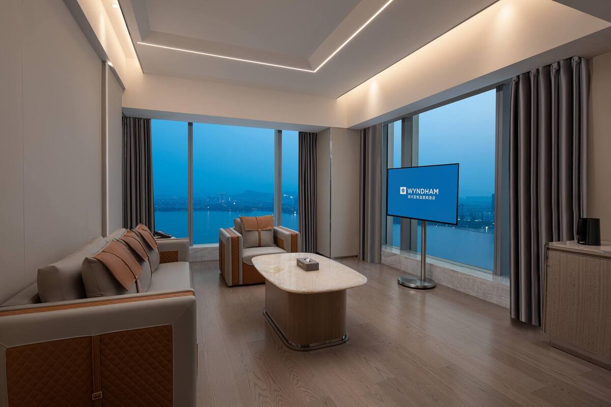 Ein modernes Hotelzimmer mit großem Fenster, einem Flachbildfernseher, einer Couch, einem Couchtisch und einem Schrank.