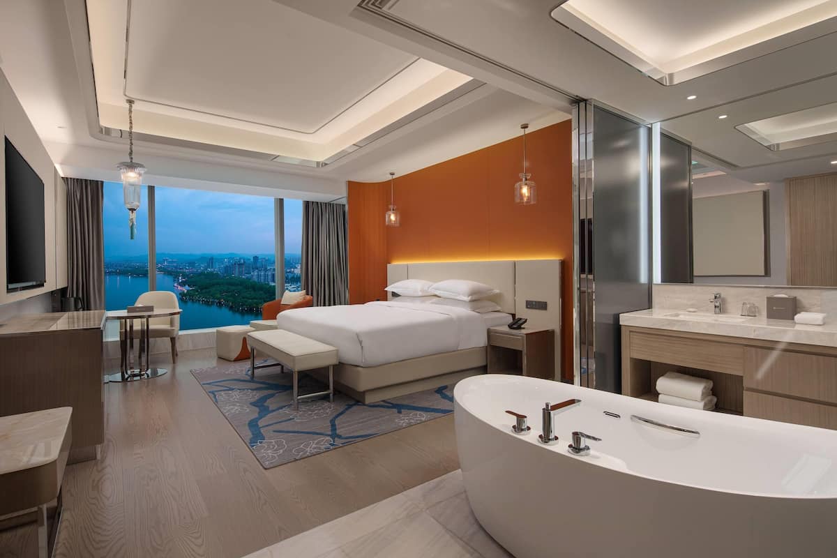 Ein modernes Hotelzimmer mit einem großen Bett, einer Sitzecke, einer Badewanne und Blick auf die Stadt.