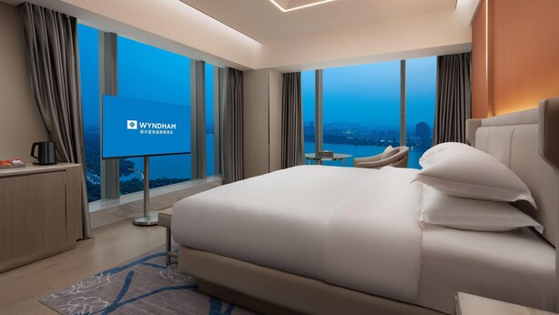 A modern hotel room with a large bed, a desk, and a TV screen displaying the Wyndham logo. - Wyndham Shaoxing Keqiao (Shaoxing)