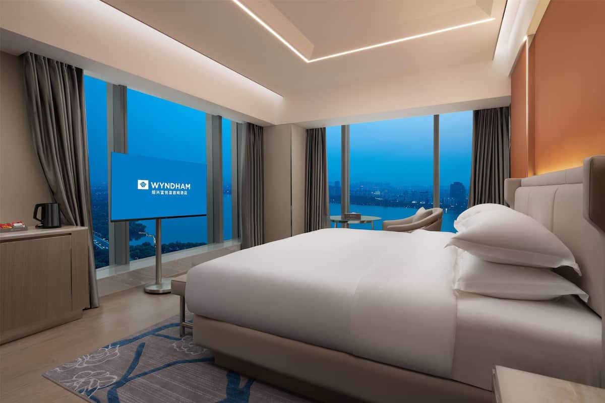 Ein modernes Hotelzimmer mit einem großen Bett, einem Schreibtisch und einem Fernseher, der das Wyndham-Logo anzeigt.