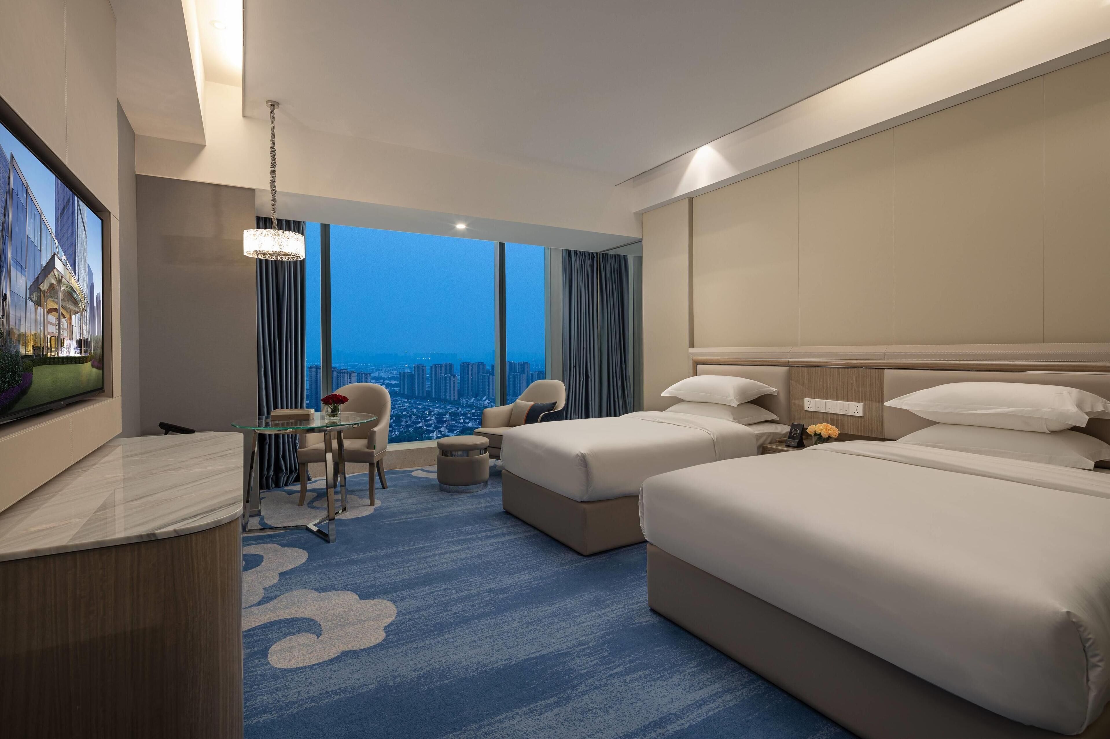 Habitación de hotel con una cama grande, un escritorio, una silla y vistas a la ciudad.