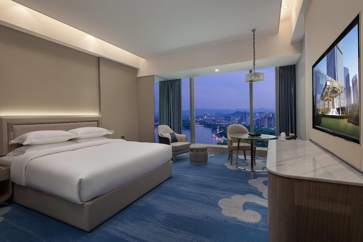 Ein Hotelzimmer mit einem großen Bett, einem Schreibtisch, einem Stuhl und einem Fernseher. Das Zimmer bietet Blick auf die Stadt.