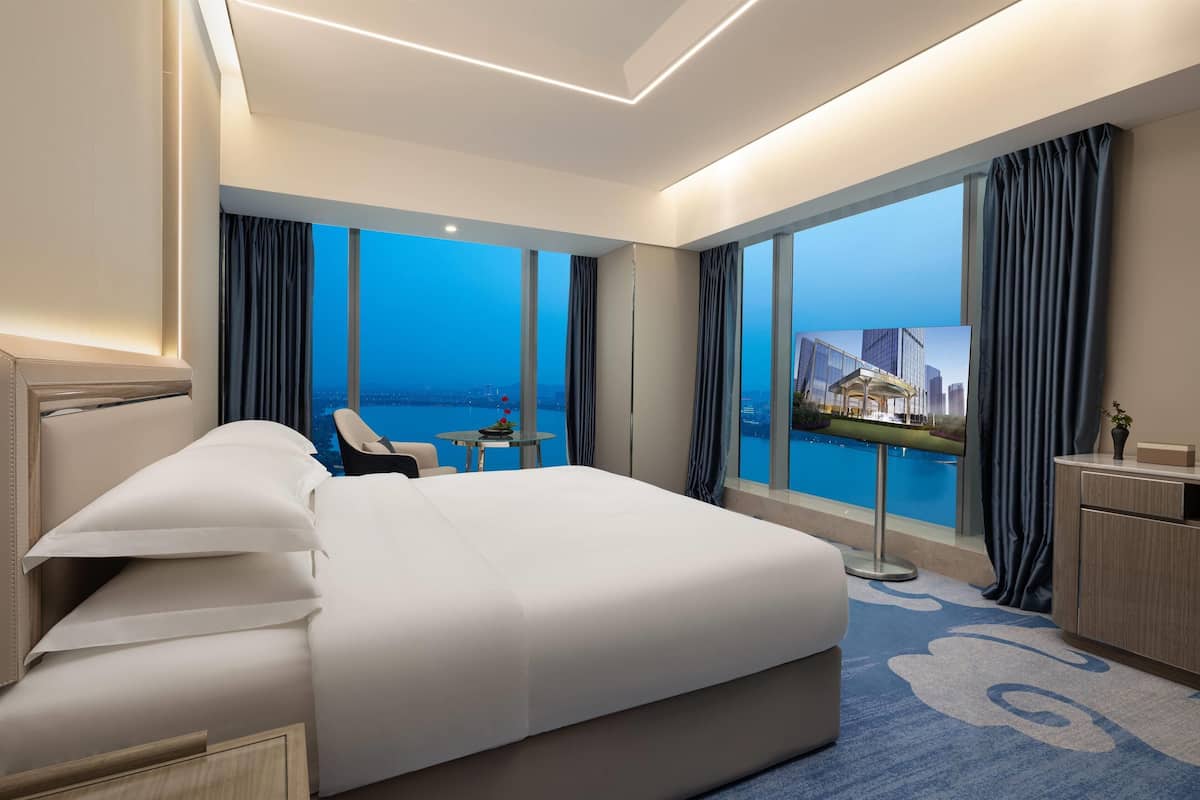 Ein modernes Hotelzimmer mit einem großen Bett, einem Schreibtisch und Blick auf Stadt und Wasser.