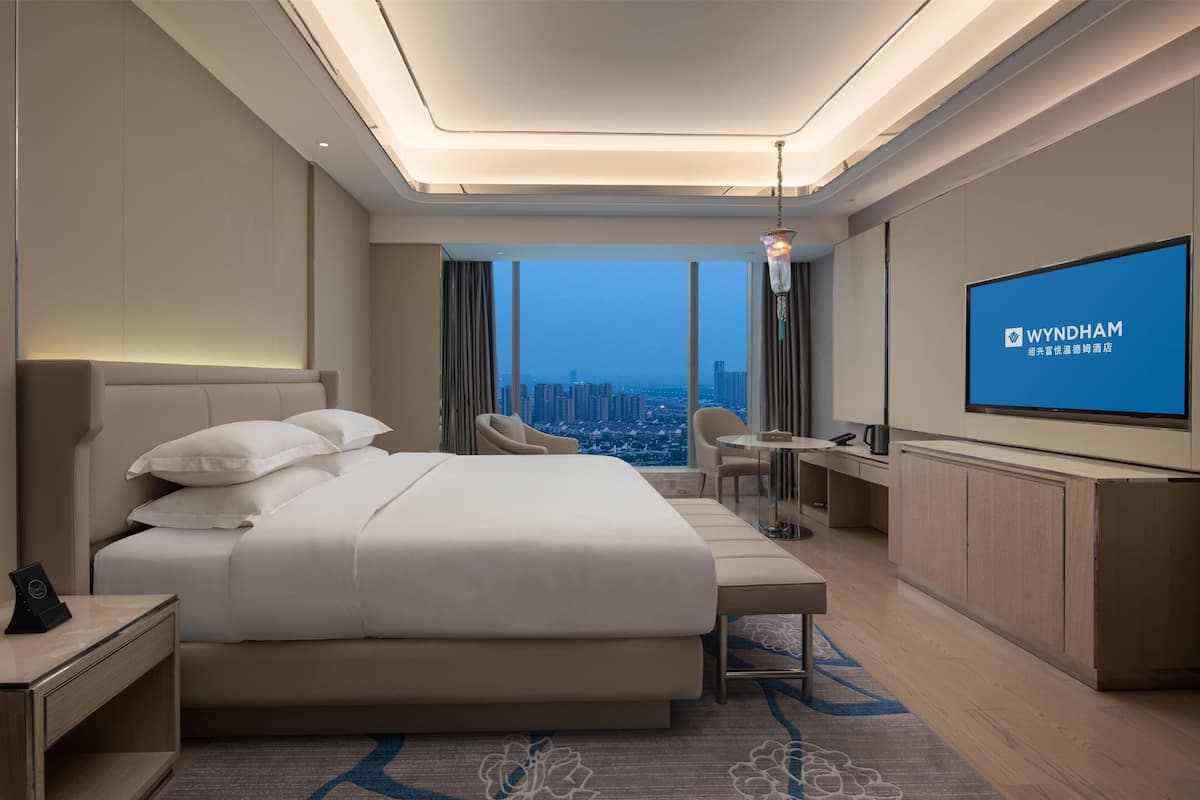 Ein modernes Hotelzimmer mit einem großen Bett, einem Schreibtisch, einem Stuhl, einem Fernseher und Blick auf die Stadt.