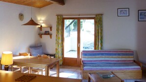 A cozy room with a wooden table, a striped sofa, a lamp, and a sliding glass door leading to an outdoor area. - Domaine de l'Espinet Villa Speranza (Quillan)