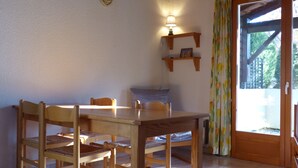 A dining area with a wooden table and chairs, a hanging light fixture, a small shelf with a picture, and a sliding glass door leading outside. - Domaine de l'Espinet Villa Speranza (Quillan)