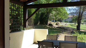 A covered patio with a table and chairs, overlooking a grassy area with trees and a stone wall. - Domaine de l'Espinet Villa Speranza (Quillan)