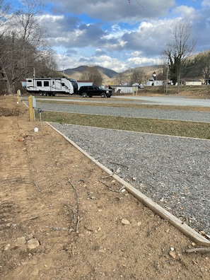 A gravel parking area with a wooden fence and a black truck parked in the background.