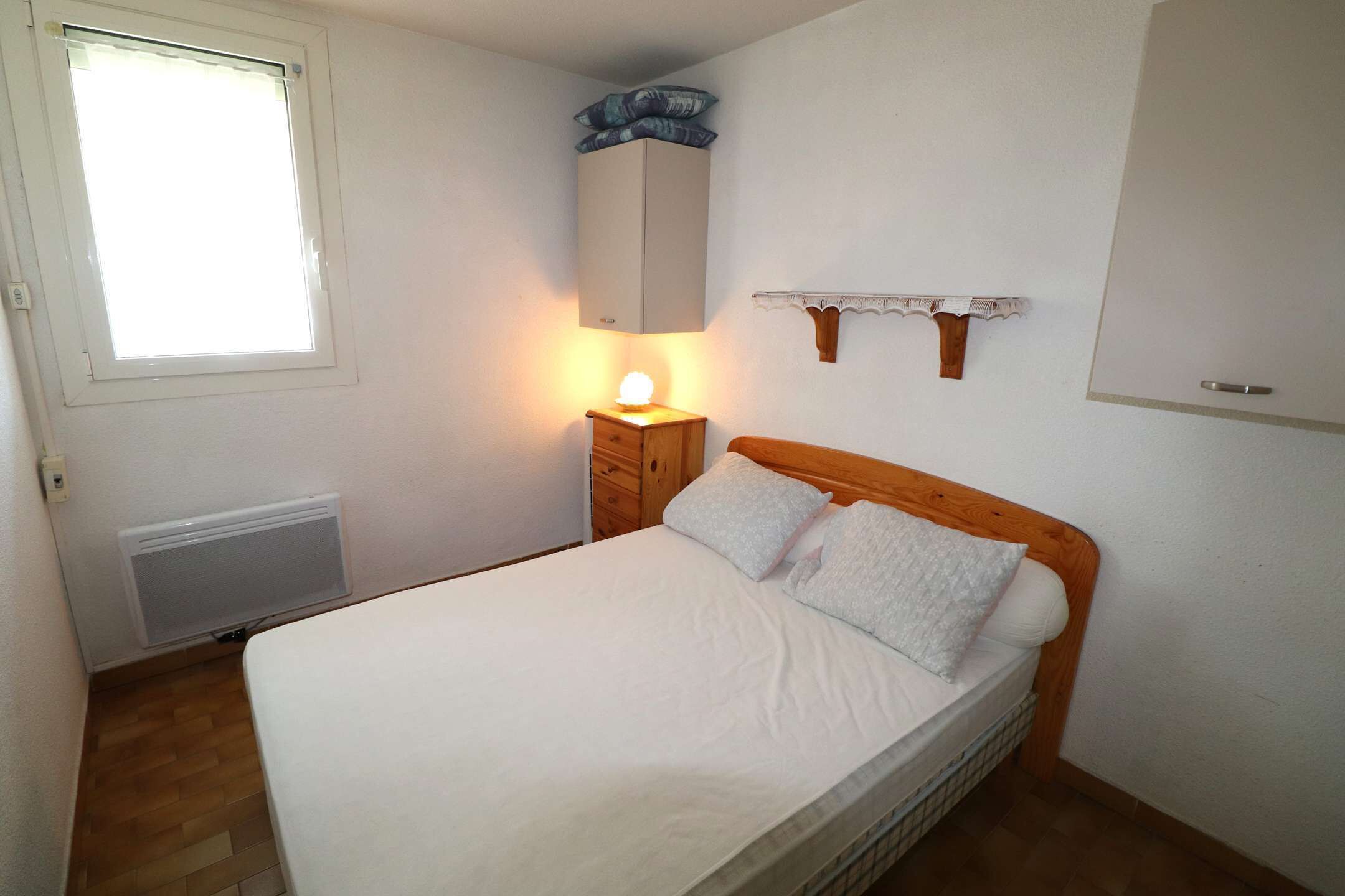 Una camera da letto con un letto, un comodino con una lampada, una finestra, un termosifone e una testiera in legno.