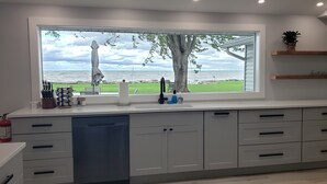 A kitchen with a large window overlooking a grassy area and the sea. There are cabinets, a sink, and a fire extinguisher. - Tranquil Lakefront home. Premium accommodations, newly remodeled (Hamlin)