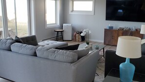 A modern living room with a grey sofa, a coffee table, a TV, and a ceiling fan. - Tranquil Lakefront home. Premium accommodations, newly remodeled (Hamlin)