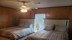Ein Zimmer mit zwei Betten, Holzwänden, einem Deckenventilator und einem Fenster mit Jalousien.