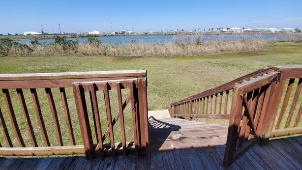 Eine Holzterrasse mit Geländern, die auf eine Wiese und ein Gewässer blickt.