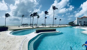 A resort pool with palm trees, beach, and a white building. - (20% OFF) Artsy & Chic Oceanfront hideaway: exclusive Cap Cana Marina district (CAP CANA)