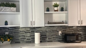 A kitchen with white cabinets, a stone backsplash, a microwave, and various potted plants.