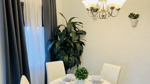 A dining area with a round table set for four, white chairs, a chandelier, and a potted plant.