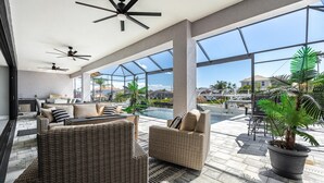 Un vaste espace de détente extérieur, aménagé avec des meubles en osier, des ventilateurs de plafond et une grande plante en pot.