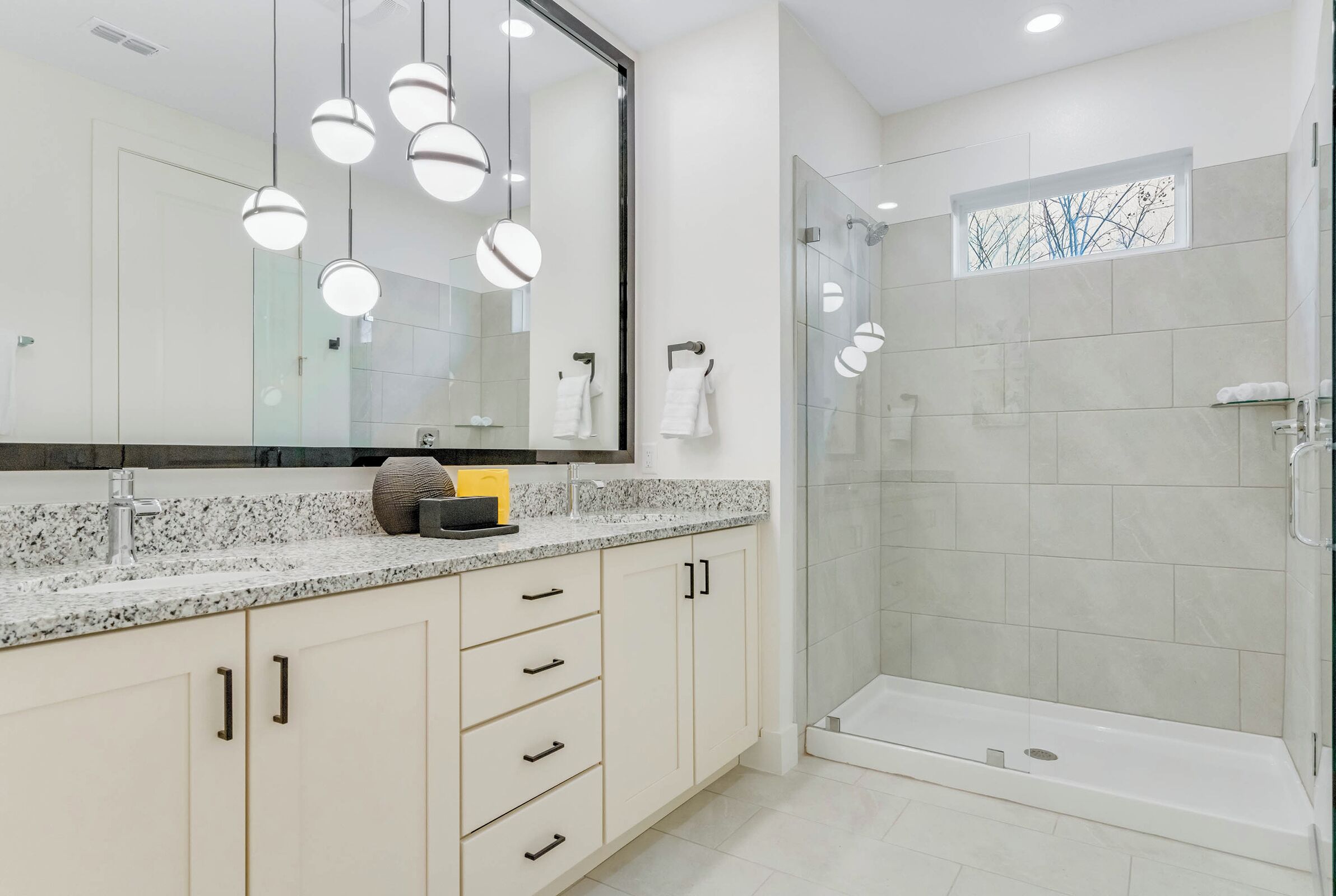 Une salle de bain moderne dotée d’un grand miroir, d’un comptoir en granit et d’une douche à parois de verre.