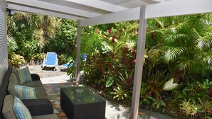 A covered outdoor seating area with a sofa and chairs, surrounded by lush tropical plants. - Tiare Taporo (Matavera District)