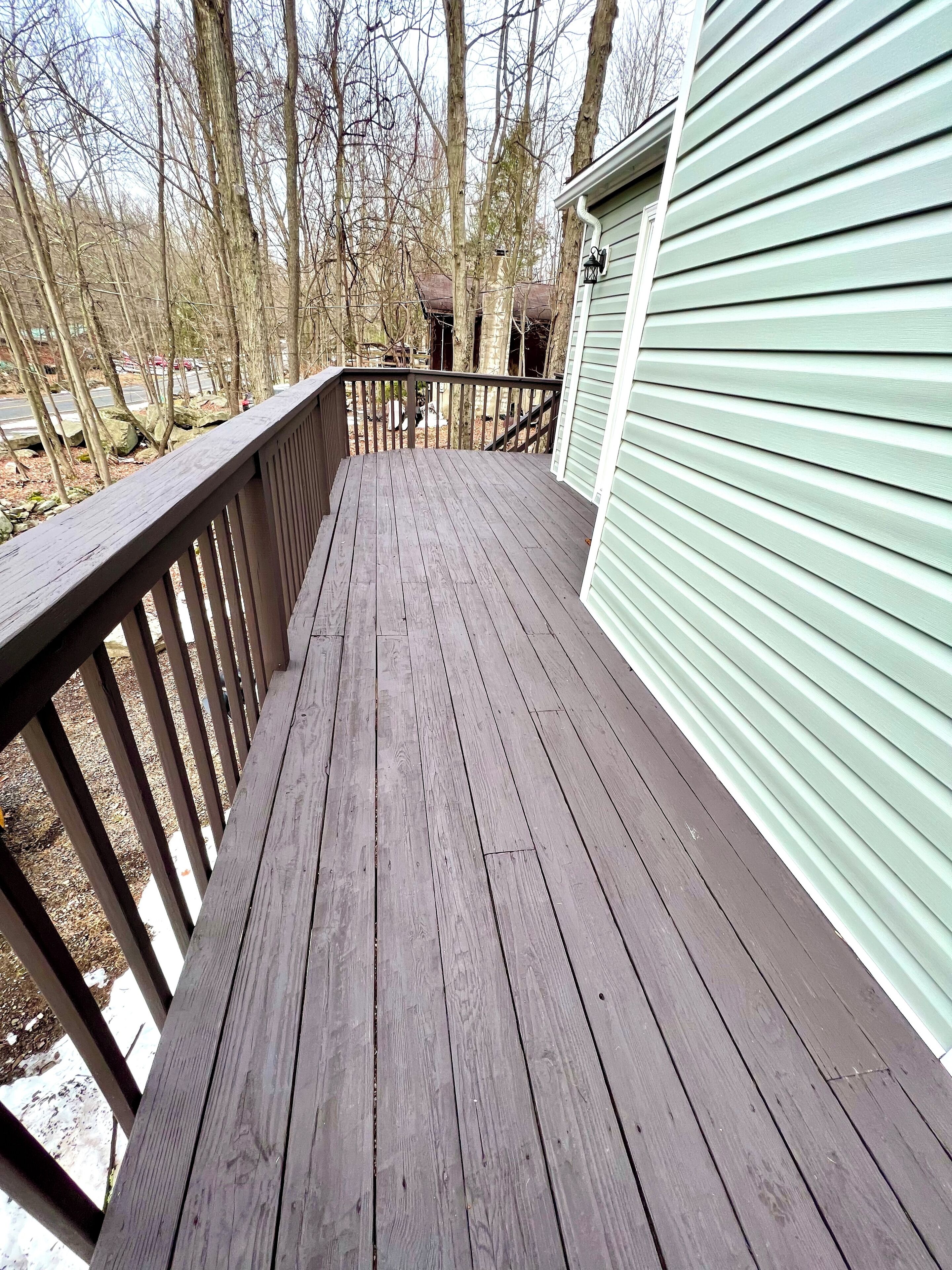 A wooden deck with a railing, leading to a green building.