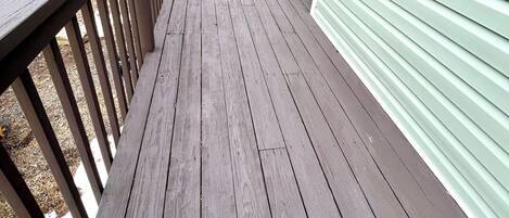 A wooden deck with a railing, leading to a green building.