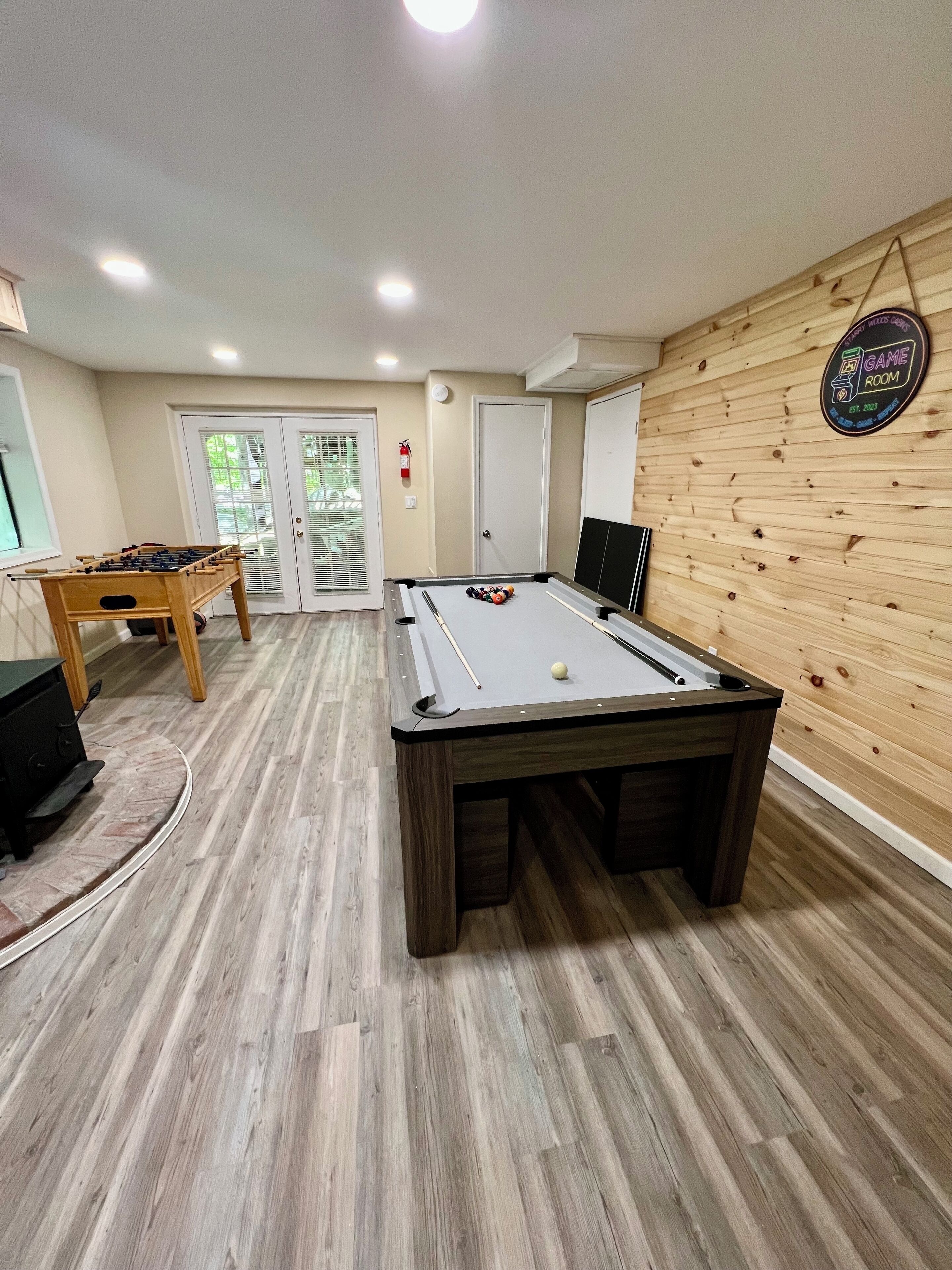 Ein Billardtisch mit Spielball, ein Kicker und ein weiterer Billardtisch in einem Raum mit Holzboden und Holzwand.