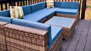 Een modulaire bank met blauwe kussens en een gestreept kussen op een houten terras.