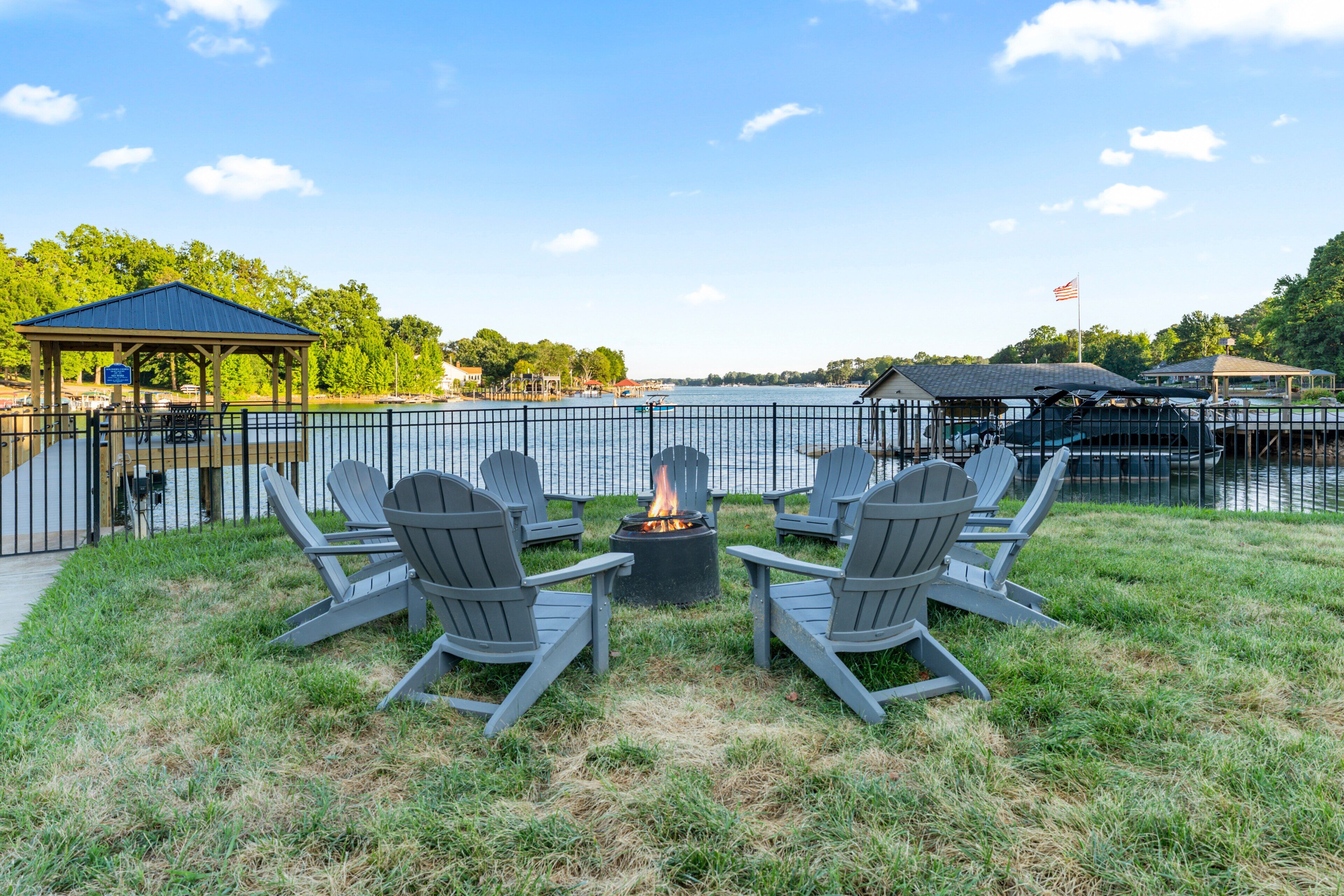 Eine Terrasse am Seeufer mit Adirondack-Stühlen, einem Feuerkorb und einem Gazebo.