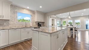 A spacious kitchen with white cabinetry, a large island, and a view of the outdoors.