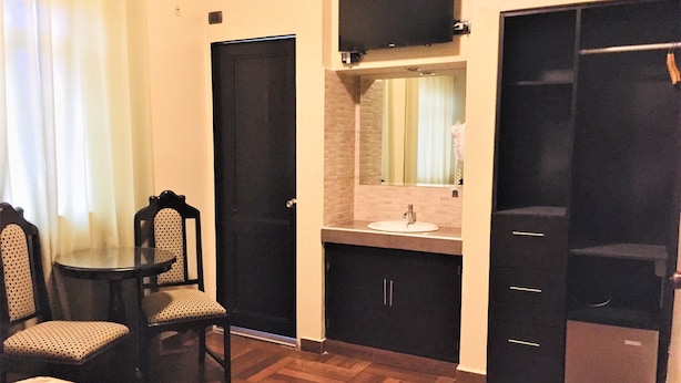 A hotel room with a bed, a small table with chairs, a bathroom with a sink and mirror, and a wardrobe. - Hostal Carlos Tenaud  (Lima)