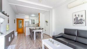 A modern living room with a grey sofa, a white coffee table, and a dining area with a table and chairs. - 2 bedroom amazing apartment in Torrevieja (Torrevieja)