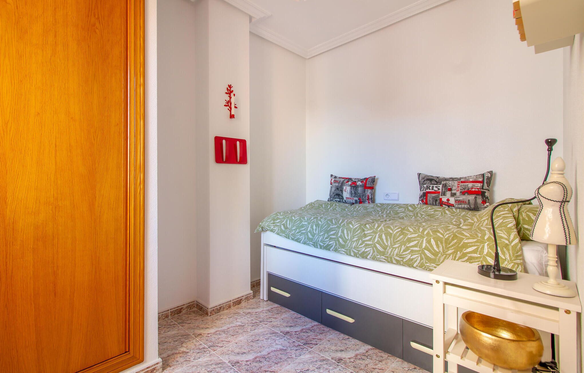 A bedroom with a bed, a nightstand, a lamp, and a decorative item on the wall.