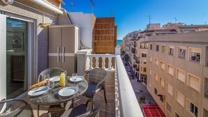 A balcony with a table set for two, a wicker chair, and a view of the sea. - 2 bedroom amazing apartment in Torrevieja (Torrevieja)