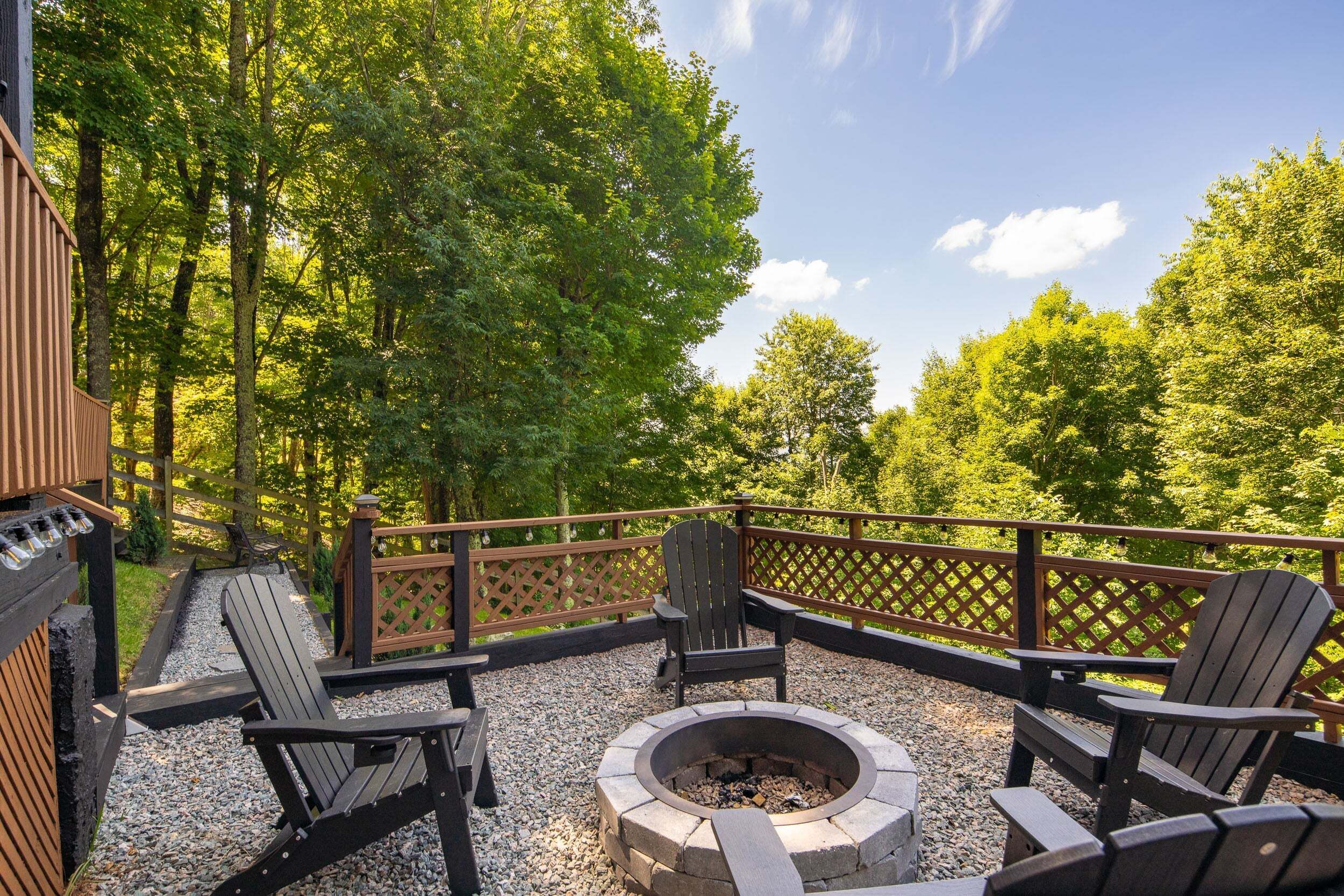 Een terras met Adirondack-stoelen, een vuurplaats en een houten omheining.