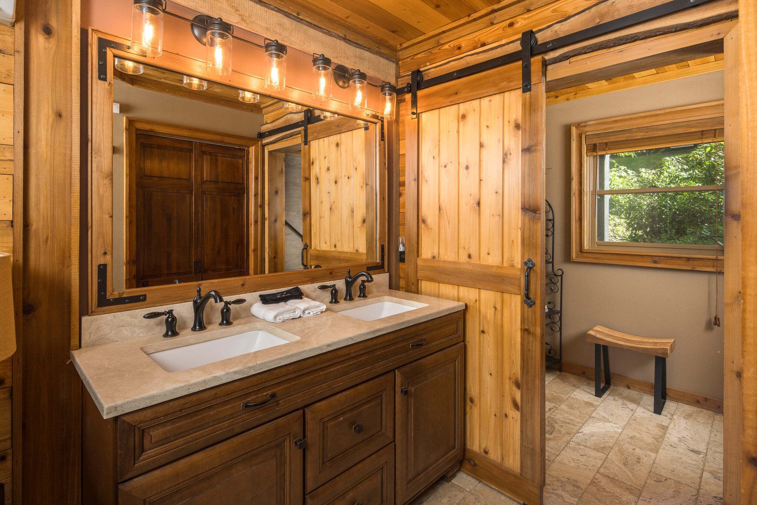 A wooden bathroom with a large mirror, two sinks, and a window.