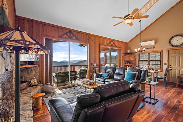 A spacious living room with a fireplace, leather seating, and a large window overlooking a scenic view.