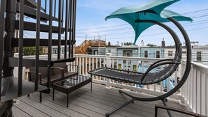 A balcony with a hammock, wicker chairs, and a grill.