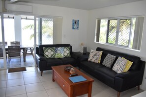 A living room with a black sofa, a wooden coffee table, and a dining area with chairs and a table. - Tupe's Beach House (Vaimaanga)