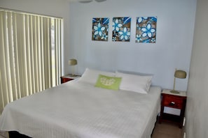 A bedroom with a large bed, two bedside tables, and three wall-mounted paintings.